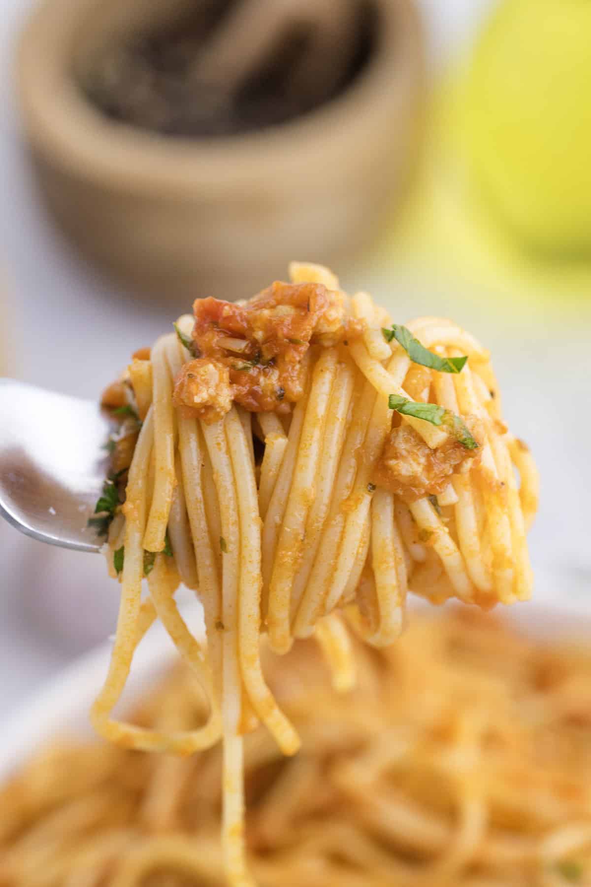 A close-up of a fork holding a twirl of spaghetti with tomato sauce and chopped herbs.