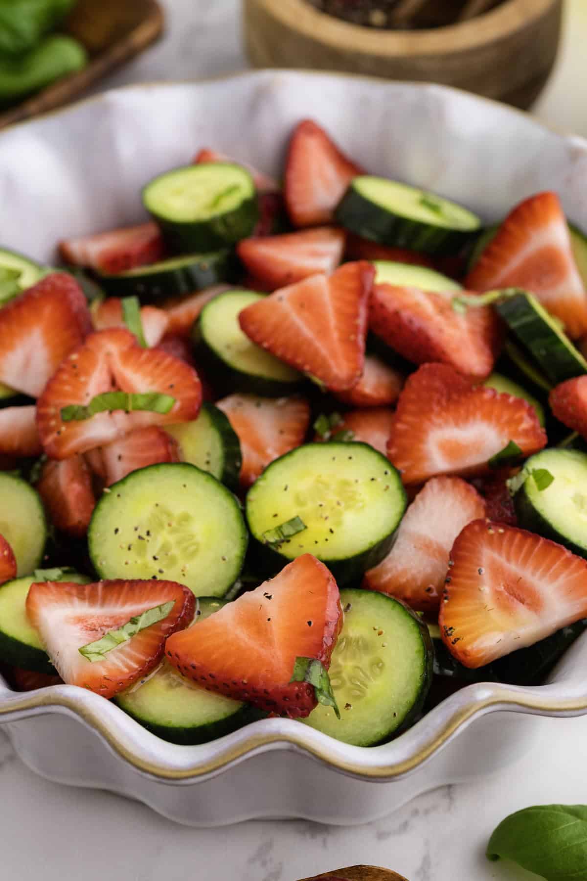 A bowl filled with sliced strawberries and cucumbers, garnished with fresh herbs and cracked black pepper.