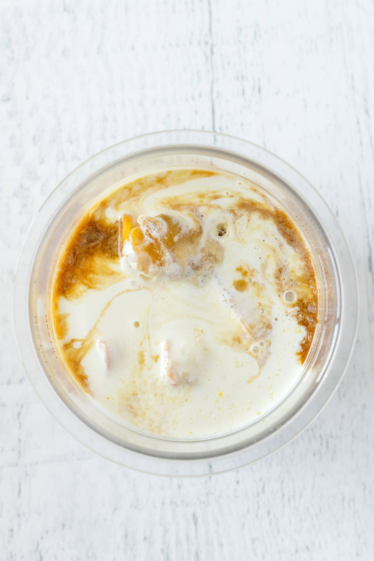 A top-down view of a clear bowl containing a mixture of creamy white liquid and orange-colored ingredient, creating a marbled effect.