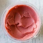 A glass bowl filled with smooth, bright pink Ninja Creami strawberry ice cream, viewed from above on a light wooden surface.