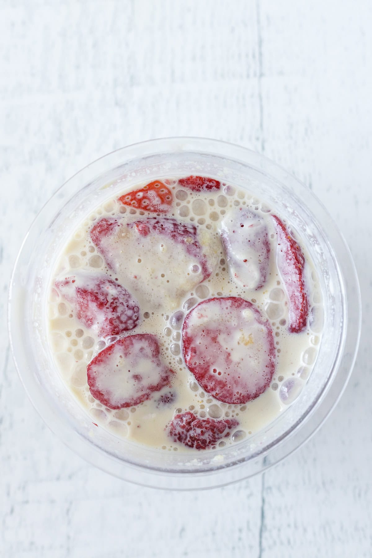 A clear cup filled with milk and sliced strawberries on a white surface, viewed from above.