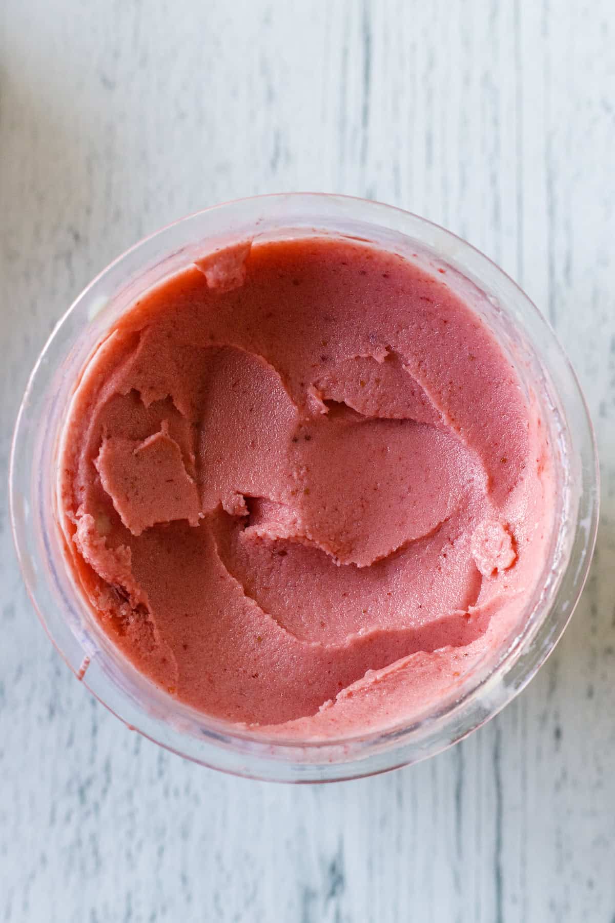 A clear container filled with pink strawberry sorbet, viewed from above on a light-colored surface.