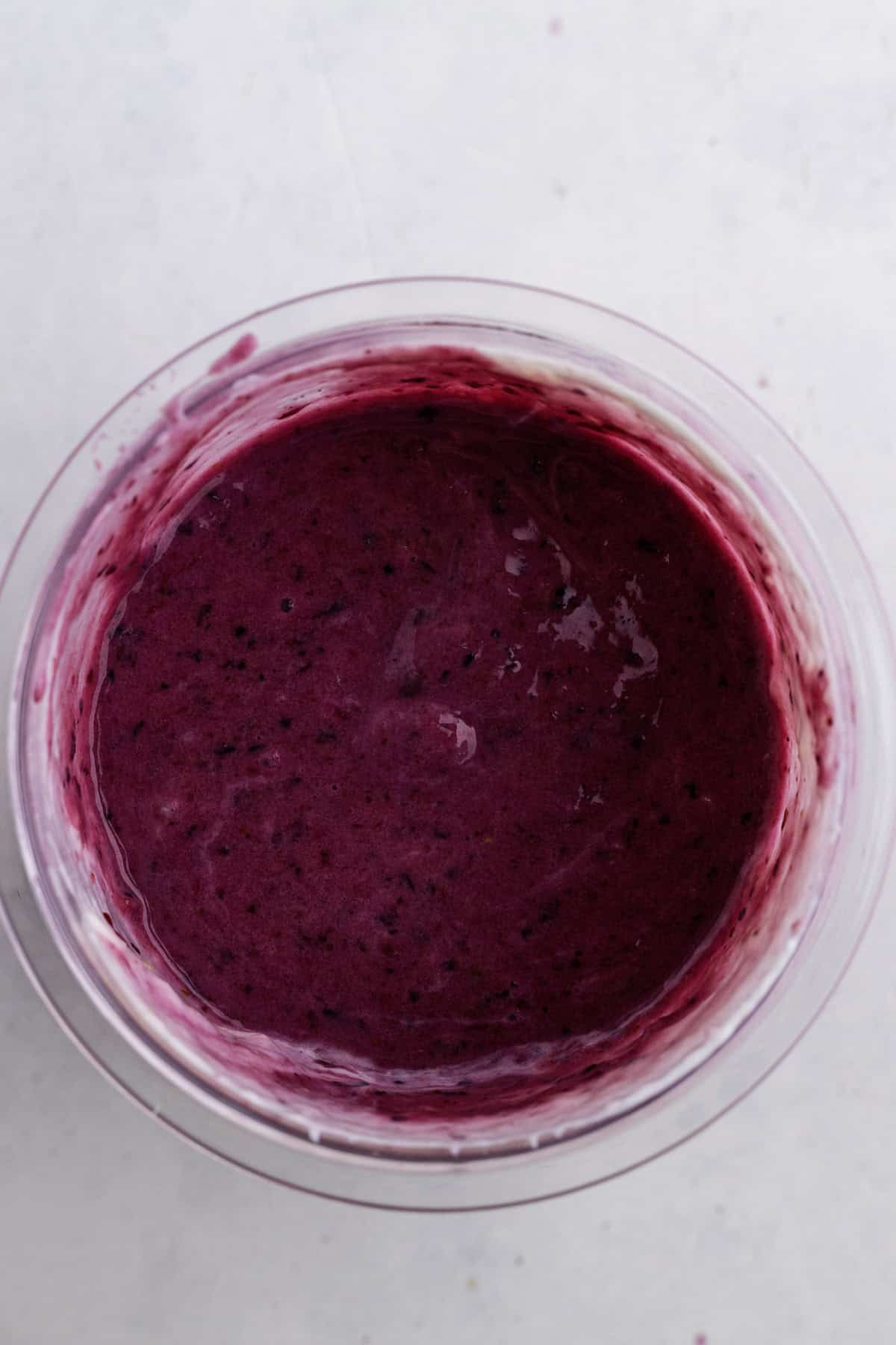 A clear bowl filled with a thick, vibrant purple smoothie mixture on a light background.