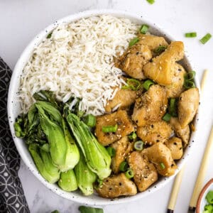 Un bol contenant du riz blanc, du bok choy sauté et des morceaux de poulet cuit garnis d'oignons verts et de graines de sésame.