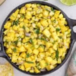 A bowl of mango corn salsa with diced mango, corn, red onion, and cilantro, seasoned with black pepper.