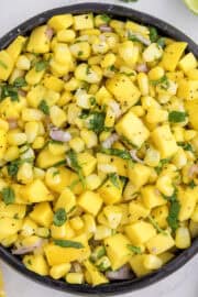 A bowl of mango corn salsa with diced mango, corn, red onion, and cilantro, seasoned with black pepper.