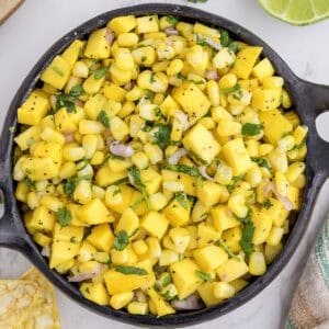 A bowl of mango corn salsa with diced mango, corn, red onion, and cilantro, seasoned with black pepper.