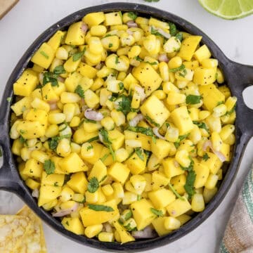 A bowl of mango corn salsa with diced mango, corn, red onion, and cilantro, seasoned with black pepper.