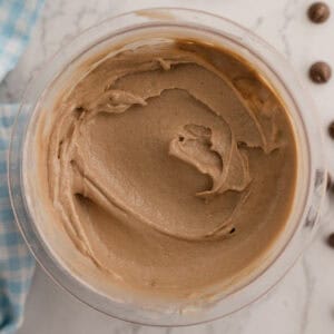 A bowl of ninja creami cottage cheese chocolate ice cream sits on a marble surface with a blue checkered napkin and chocolate pieces nearby.