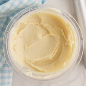 Un bol de crème glacée protéinée à la vanille est posé à côté d'un tissu à carreaux bleus et blancs sur une surface blanche.
