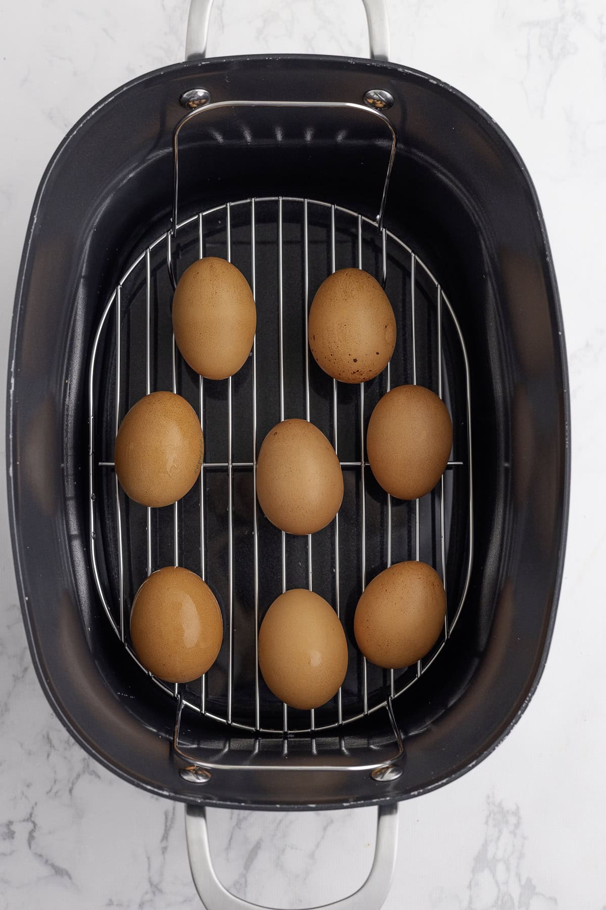 Eight brown eggs are arranged on a metal rack inside a Ninja Foodi possible cooker, viewed from above.