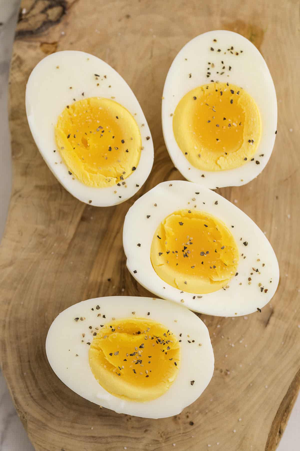 Four halved boiled eggs with slightly soft yolks are sprinkled with black pepper and arranged on a wooden surface.