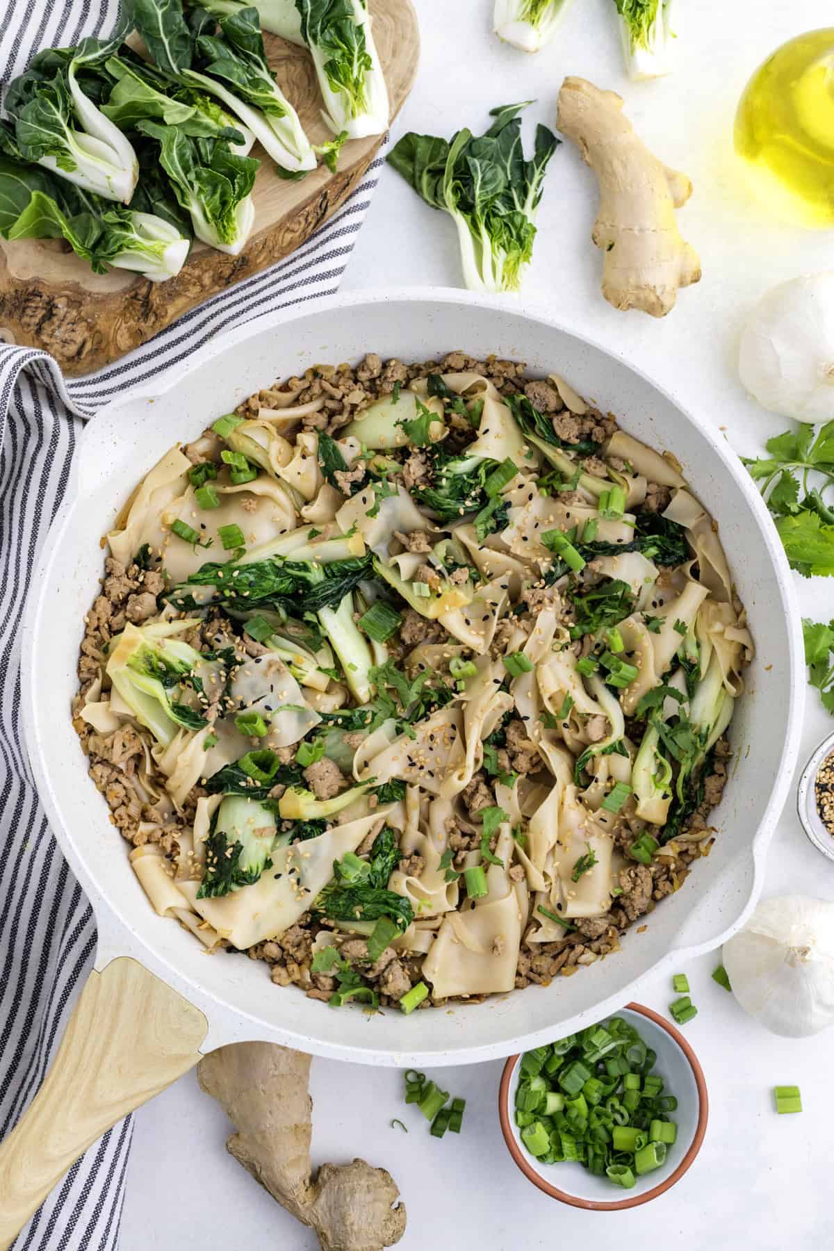 A white pan filled with a noodle dish containing ground meat, bok choy, and sesame seeds.