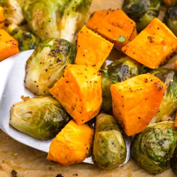 Roasted Brussels sprouts and sweet potato cubes on a metal spatula, seasoned with black pepper and herbs.