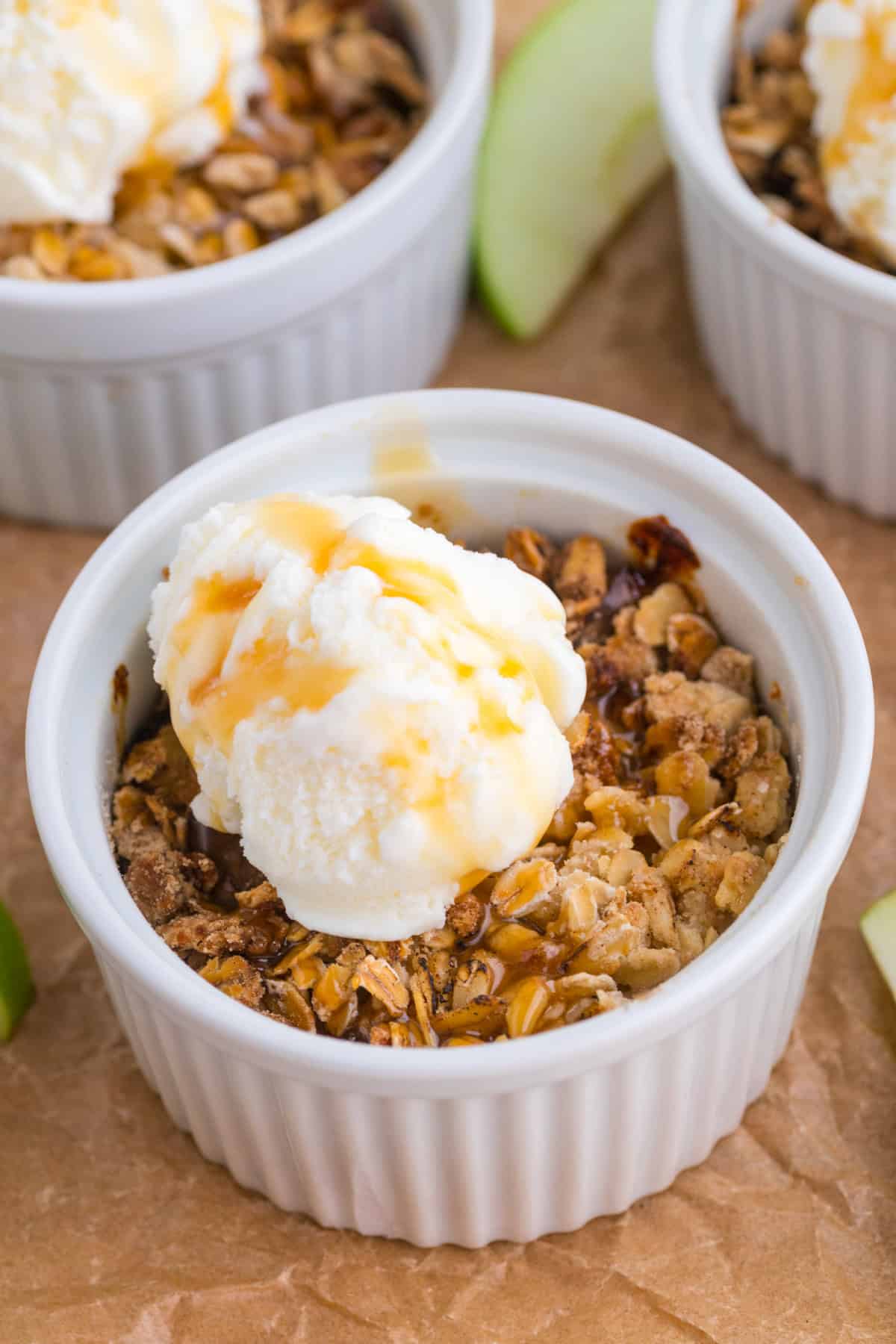 Un petit ramequin blanc rempli de crumble aux pommes, garni d'une boule de glace à la vanille et nappé de sauce au caramel.
