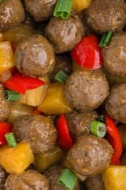 Meatballs mixed with pineapple chunks, red bell pepper pieces, and chopped green onions.