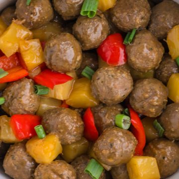Meatballs mixed with pineapple chunks, red bell pepper pieces, and chopped green onions.